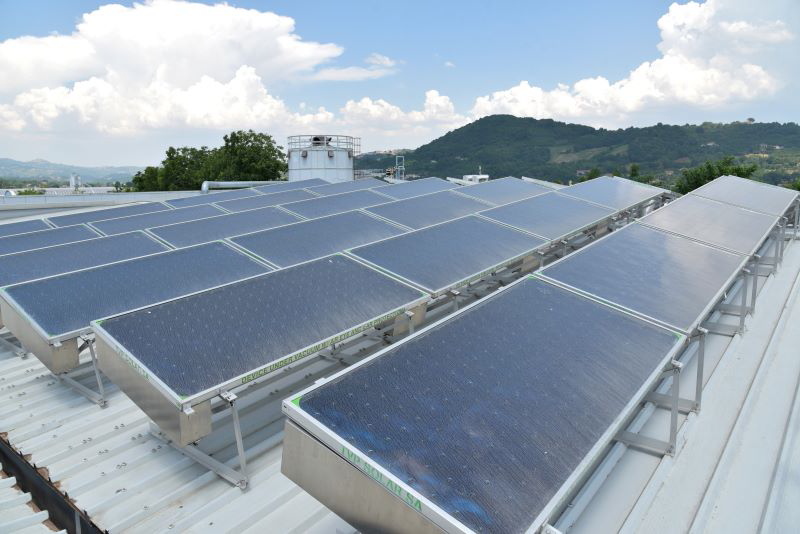 Auf einem Industriedach stehen Solarthermiekollektoren und ein Wasserspeicher. Im Hintergrund grüne Hügel.