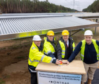 Vier Männer mit gelben Westen drücken auf einen roten Knopf, um eine große Solarthermieanlage für Prozesswärme in Betrieb zu nehmen. Sie ist hinter ihnen.