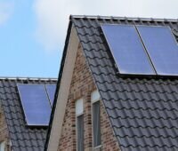Im Bild zwei Häuser mit Solarkollektoren, in den technischen FAQ der BEG-Förderung ist festgelegt wie groß die Kollektorfläche sein muss, um den Klimageschwindigkeits-Bonus für Biomasseheizungen zu erhalten.