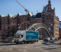 LKW mit Solarwatt-Schriftzug fährt über historische Brücke vor alten Backsteinhäusern - PV-Installation in Hamburg