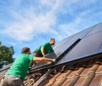 Arbeiter installieren auf einem Spitzdach neue Solarstrommodule.
