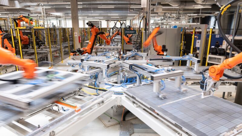 Blick in eine Photovoltaik-Produktion mit roten Roboterarmen und Modulen.
