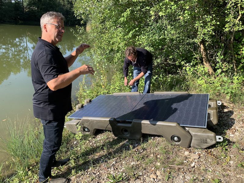 Zwei Männer und zwei Photovoltaik-Module auf einer Kunststoff-Konstruktion am Ufer - die Floating-PV-Anlage geht in den Test.