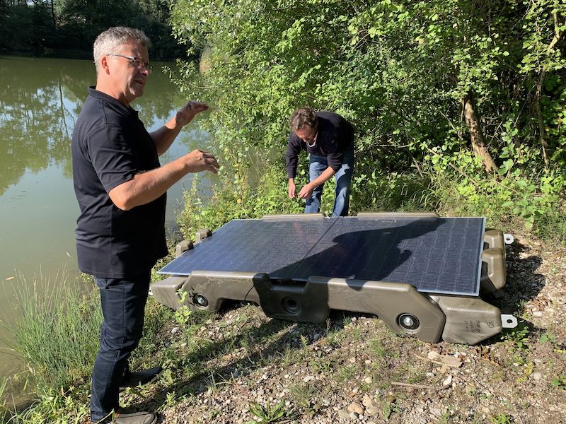 Zwei Männer und zwei Photovoltaik-Module auf einer Kunststoff-Konstruktion am Ufer - die Floating-PV-Anlage geht in den Test.