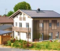 Einstöckiges Einfamilienhaus mit Solarthermieanlage an Dach und Fassade.