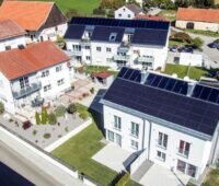 Luftbild von drei Mehrfamilienhäusern, von denen zwei Solarthermie und PV nutzen.