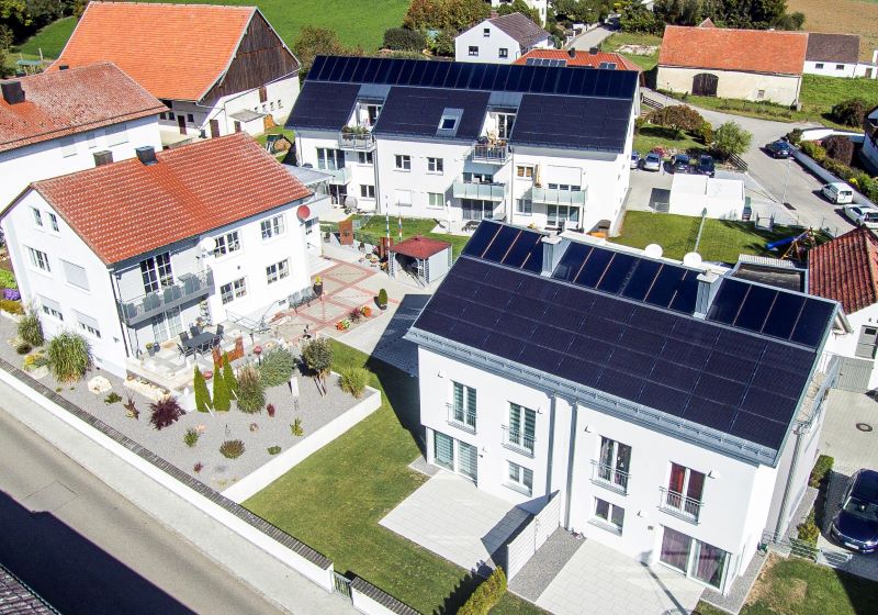 Luftbild von drei Mehrfamilienhäusern, von denen zwei Solarthermie und PV nutzen.