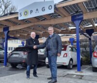 Zwei Männer stehen vor Solar-Carport auf Parkplatz und schütteln sich die Hand.
