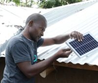 Zu sehen ist ein Mann in Afrika bei der Installation eines kleinen PV-Moduls. „Startup Energy“ ist für Projektideen in Deutschland und Ostafrika gedacht.