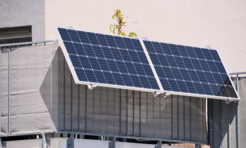 Steckersolargerät an einem Balkon montiert, Solarmodul am Geländer befestigt und über Kabel mit der Wohnung verbunden.