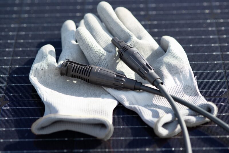 Ein paar Handschuhe und zwei Teile eines Steckverbinders auf einem Photovoltaik-Modul