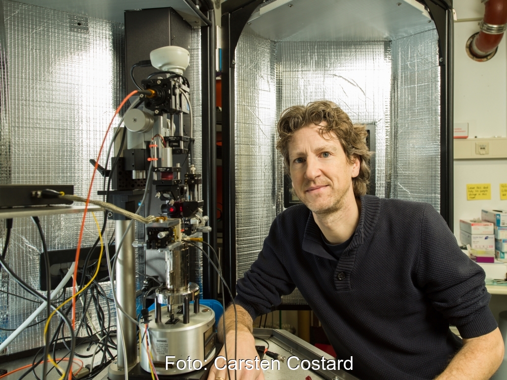 Ein technisches Gerät mit vielen Drähten - das Photovoltaik-Mikroskop - und ein Mann daneben.