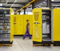 Gelbe Schaltschränke in einer Fertigungshalle der Schaper Gruppe, die gerade Batterie-Speicher von Tesvolt für Wasserstoff-Projekte eingekauft hat.