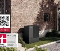 Eine schwarze Wärmepumpe steht vor einer geklinkerten Hausfassade.