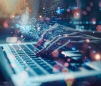 Hände tippen auf einem Laptop, darüber schweben Zeichen und Symbole - als Viusalisierung der Digitalisierung.