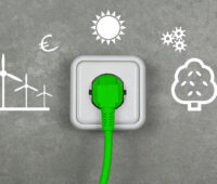 Graue Wand mit Symbolen für Windenergie, Sonne, Bioenergie und eine Steckdose mit einem grünen Stecker - Symbolbild für klimaneutrales Stromsystem