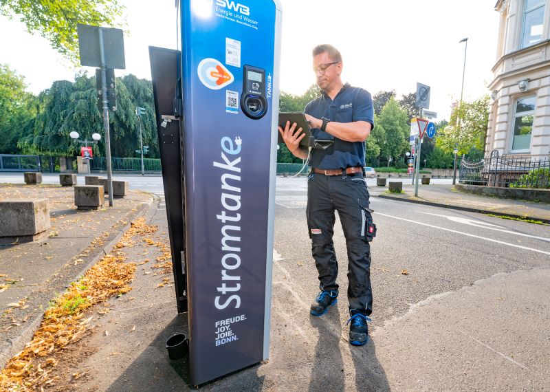 Ein Mitarbeiter der Stadtwerke Bonn checkt eine Ladesäule an einer Straße.