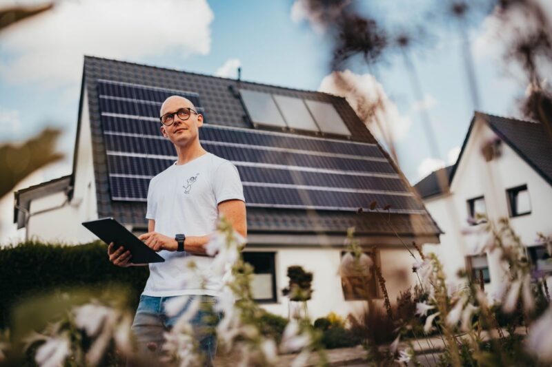 Ein Techniker mit einem Pad in der Hand vor einem Einfamilienhaus mit Dach-PV.