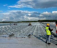 Im Bild Monteure auf einem Flachdach, die das Supra-Photovoltaik-Montagesystem von Sunbeam aufbauen.