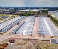 Luftbild von großem Batteriespeicherpark am Rande eines Kanals und eines Gewerbegebietes.
