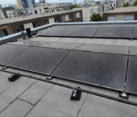 Auf einem Flachdach installierte PVT-Module in einem Wohnquartier. Die dunklen Hybridmodule sind in mehreren Reihen montiert. Im Hintergrund sind weitere Wohngebäude des Quartiers zu sehen.