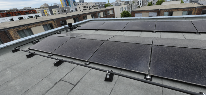 Auf einem Flachdach installierte PVT-Module in einem Wohnquartier. Die dunklen Hybridmodule sind in mehreren Reihen montiert. Im Hintergrund sind weitere Wohngebäude des Quartiers zu sehen.