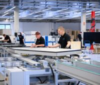 Frauen udn Männer an einer Produktionslinie für PVT-Module bei Sunmaxx.