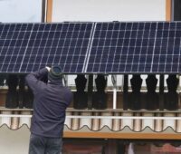 Im Bild ein Mann, der ein Balkonkraftwerk installiert. Die Balkonsolar-Petition an den Bundestag setzt sich für Erleichterungen ein.