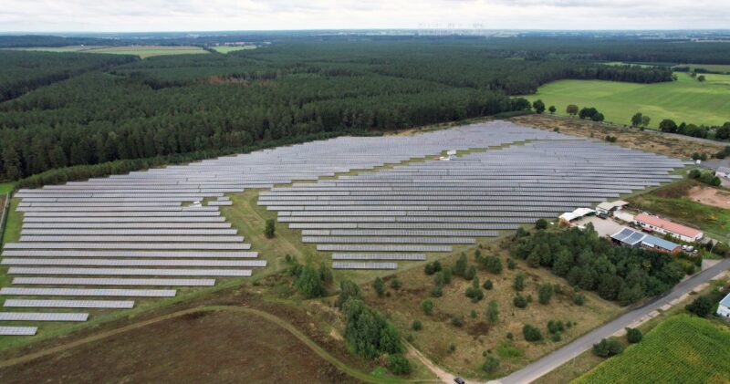 Luftbild eines PV-Parks am Waldrand im Flachland.