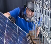 Zu sehen ist ein Teststand beim TÜV Rheinland, auf dem ein Mitarbeiter ein Photovoltaik-Modul auf die Beständigkeit gegenüber Schneelasten prüft.