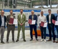 Wissenschaftler stehen aufgereiht mit Minister im LIKAT, sie erforschen den Wasserstofftransport mit Formiatsalz.
