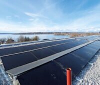 Blick über PVT-Solarmodule auf einem Flachdach im Vordergrund, im Hintergrund der Ammersee in Herrsching.