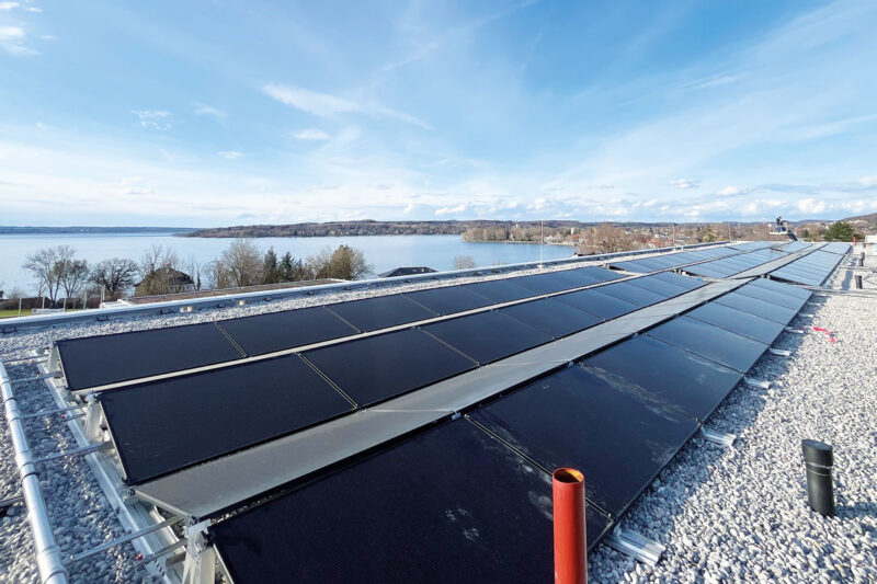 Blick über PVT-Solarmodule auf einem Flachdach im Vordergrund, im Hintergrund der Ammersee in Herrsching.