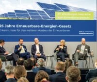 Blick auf eine Diskussionsrunde - fünf Personen auf einer Bühne. Im Hintergrund ein Plakat zu 25 Jahre Erneuerbare-Energien-Gesetz (EEG).