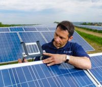 Ein Mitarbeiter des TÜV-Rheinland steht mit einem Messinstrument in einer PV-Freianlage.
