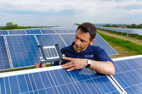 Ein Mitarbeiter des TÜV-Rheinland steht mit einem Messinstrument in einer PV-Freianlage.