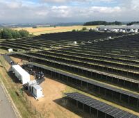 Vogelperspektive auf Photovoltaik-Großanlage und einen Container, in dem sich ein Batterie-Speicher befindet.