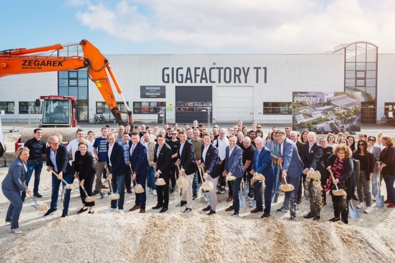 Mehrere Dutzend Personen mit Spaten vor Baustelle einer neuen Fabrik.