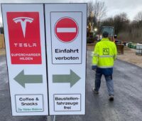 Ladepark Hilden: Zu sehen ist ein Schild, das zu den provisorisch aufgestellten Tesla-Superchargern führt.