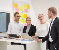 Mehrere Personen hören einem Vortragenden mit Laptop zu. Es geht um Beratung.