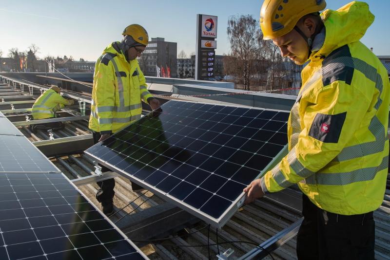 Arbeiter installieren Solarmodule auf einem Tankstellendach.