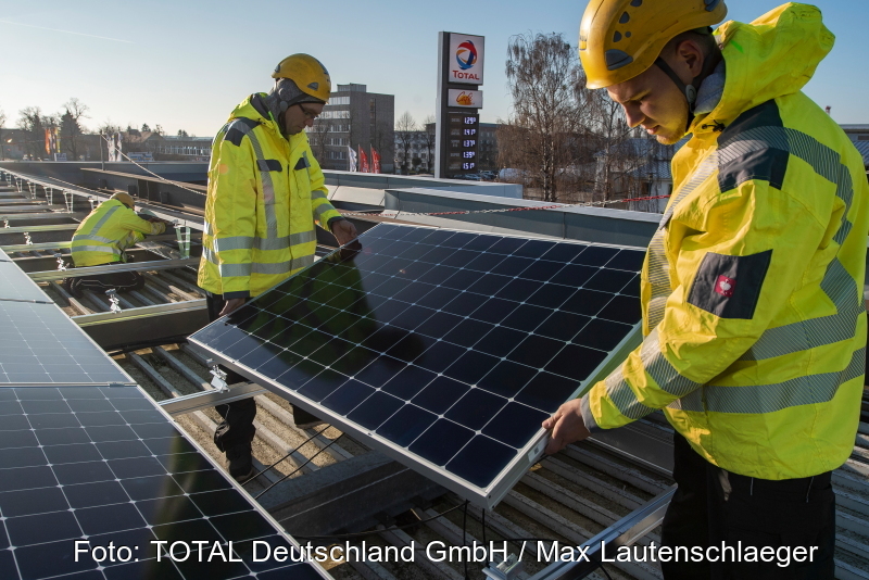 Arbeiter installieren Solarmodule auf einem Tankstellendach.