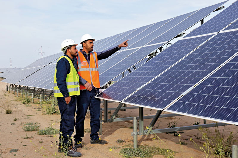 Zwei Arbeiter mit Signalwesten vor Photovoltaikmodulen Eines PV-Parks in Tunesien