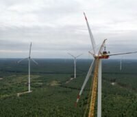 Ein Windpark in waldigem Gebiet mit Autobahn und einem Arbeiter in der Gondel.