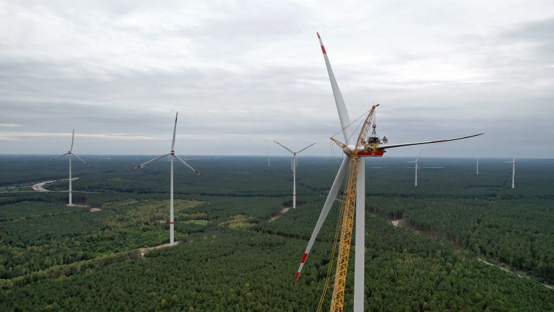 Ein Windpark in waldigem Gebiet mit Autobahn und einem Arbeiter in der Gondel.