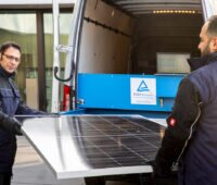 Zwei Männer heben PV-Modul in mobiles Prüflabor für Test