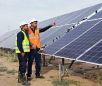 Zwei tunesische Arbeiter an einer Reihe von PV-Modulen einer Freiflächenanlage.