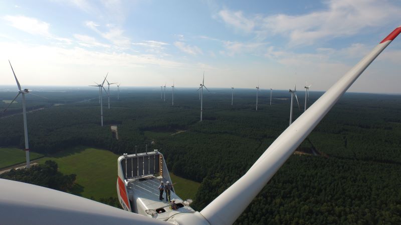 Ein Windpark in Deutschland von oben. Auf einer der Gomdeln stehen zwei Menschen