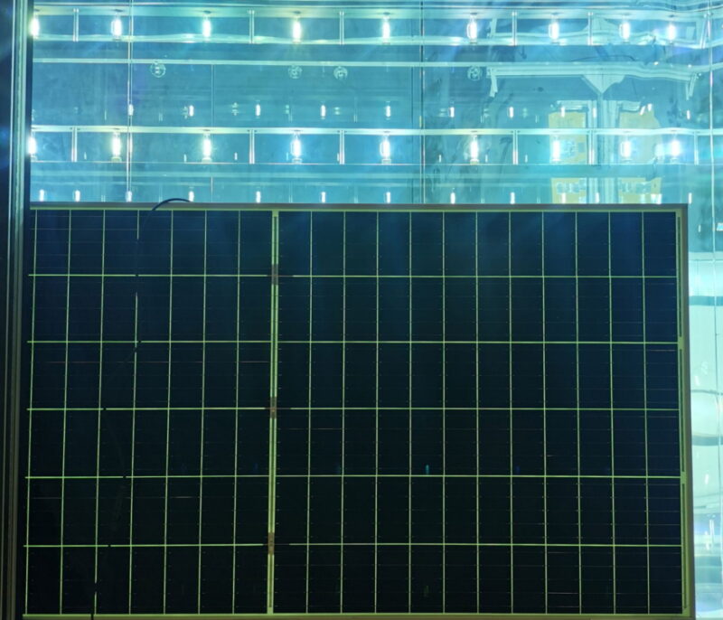 Aufrecht stehendes Solarmodul, das rückwärtig von UV-Licht bestrahlt wird.