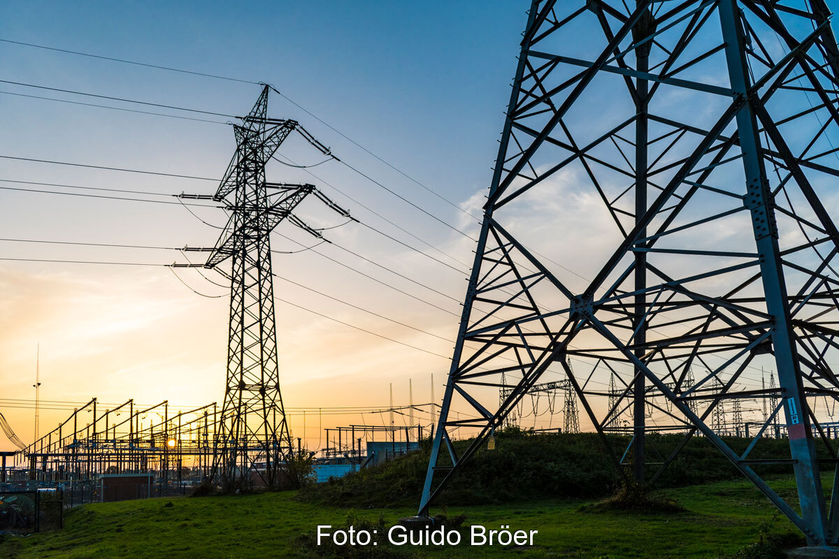 Sonnenuntergang hinter einem Umspannwerk. Im Vordergrund Hochspannungsmasten.